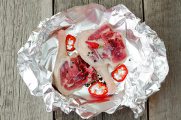 Raw duck leg in foil with vegetables and spices on a wooden table. Cooking meat