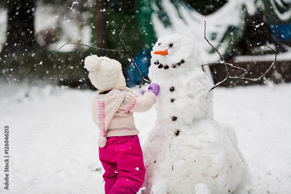 Falling Snow Toque A toddler girl in a pink snowsuit with wooly hat toque builds a large ...