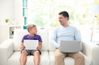 © Africa Studio - Little son with tablet and father with laptop sitting on sofa at home