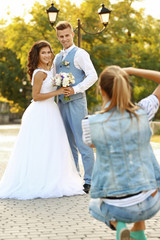 Wall Mural - Young woman taking photo of happy wedding couple in park