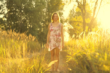 Woman in a dress walking along the summer forest path in the sunlight