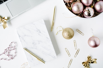feminine workspace with laptop, marble diary, golden pen, christmas decoration, christmas balls, tinsel, bow on white background. flat lay, top view