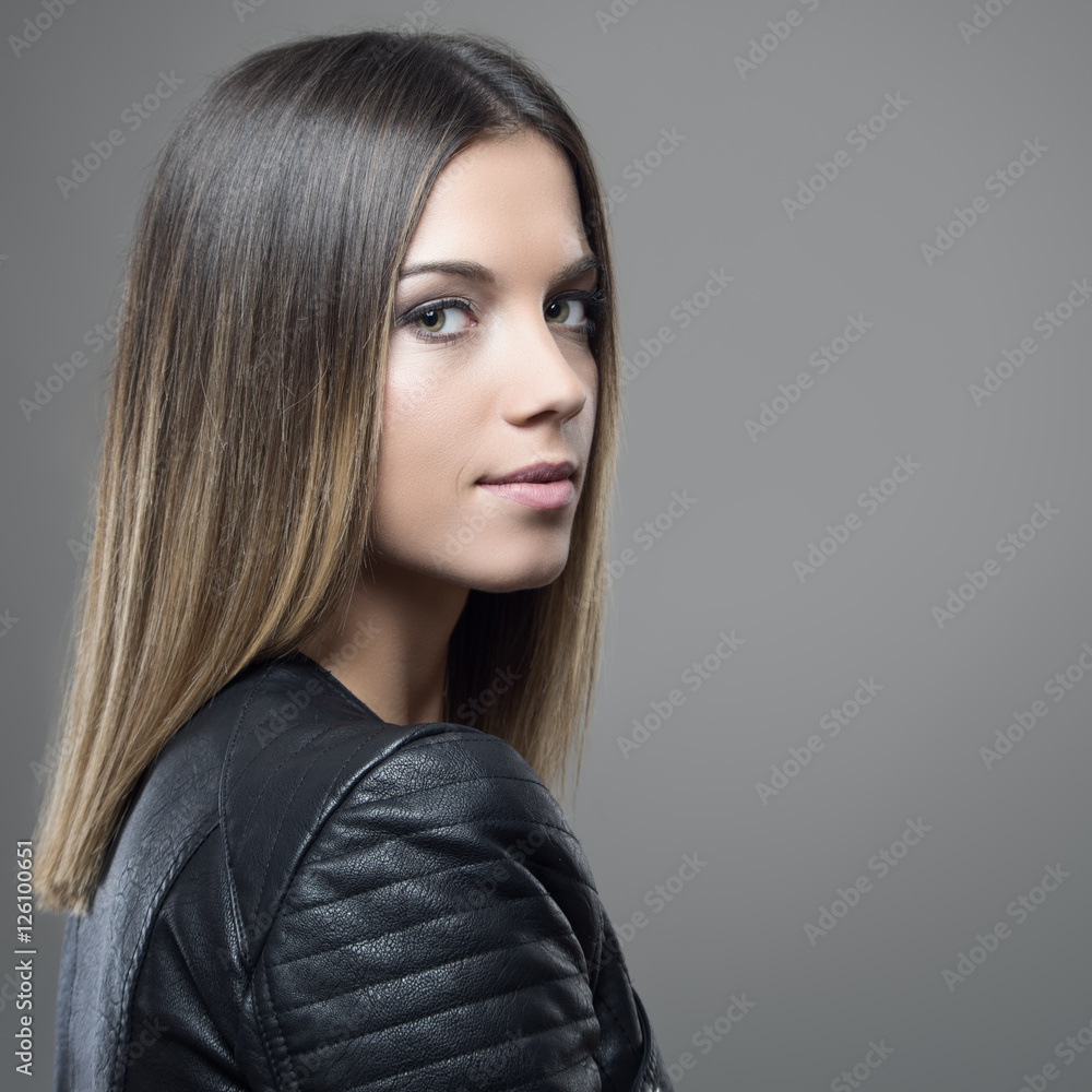 Portrait of young beautiful woman with ombre straight hairstyle looking at camera over the shoulder on gray studio background with copyspace