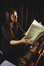 Young Woman Looking At Sheet Music While Playing A Piano