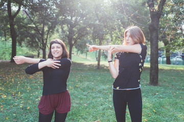 Two young beautiful caucasian women stretching outdoor in a city park in sunny day - sportive, training, wellness concept