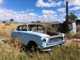 Rusty old abandoned blue car in overgrown grass field