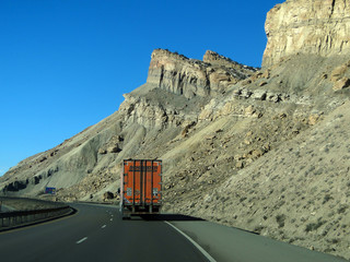 GRAND JUNCTION, COLORADO - JAN 28 - Orange semi truck drives past cliffs on Interstate I-70 near Grand Junction, Colorado