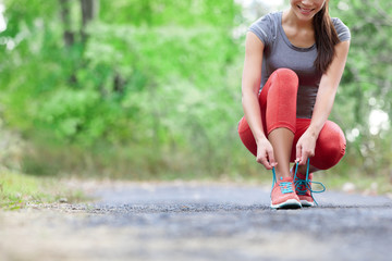 Wall Mural - Running shoes - closeup of woman tying shoe laces. Female sport fitness runner getting ready for jogging outdoors on forest path in summer season.