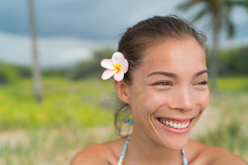 Hawaii Asian girl wearing plumeria flower hair accessory. Fresh real natural pink plumeria flower, a polynesia typical decoration. Happy smiling woman wearing a hawaiian typical flower in her hair.