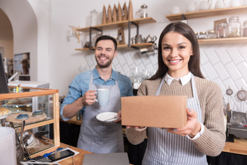 Charming smiling waiters holding cup and box.