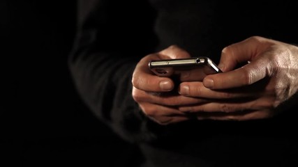 Footage of a man typing a message on his mobile phone, isolated on a black background....