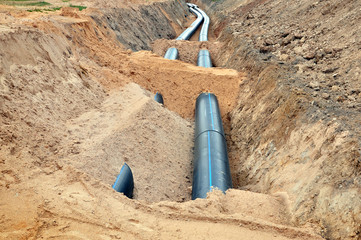 The process of laying of engineering and heating systems. Two black plastic pipes are in a trench of sand in perspective.