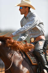 Wall Mural - Portrait of a rider in cowboy chaps, boots and hat on a horseback performs an exercise during a competition