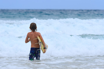 Young Surfer with surfboard going to the sea at surf spot.