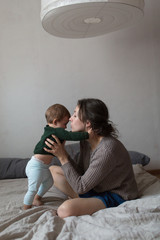 Wall Mural - young mother and baby in  knit sweaters playing on  bed, concept