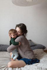 Wall Mural - young mother and baby in  knit sweaters playing on  bed, concept