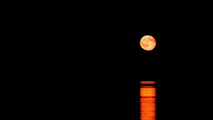 a timelapse shot of a full moon rising above the ocean surface casting a beautiful reflection that g