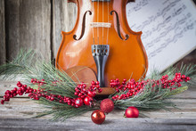 Horizontal Image Of The Bottom Half Of A Violin With Sheet Music And Christmas Fern And Cranberries Adorning The Front Of The Fiddle On Rustic Wood Background.