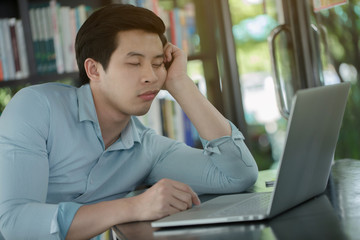 Sleepy young Asian worker with laptop computer