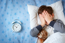 Six Years Old Child Sleeping In Bed On Pillow With Alarm Clock And A Teddy Bear