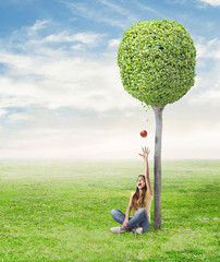 Wall Mural - young woman being surprised by a red apple under a tree