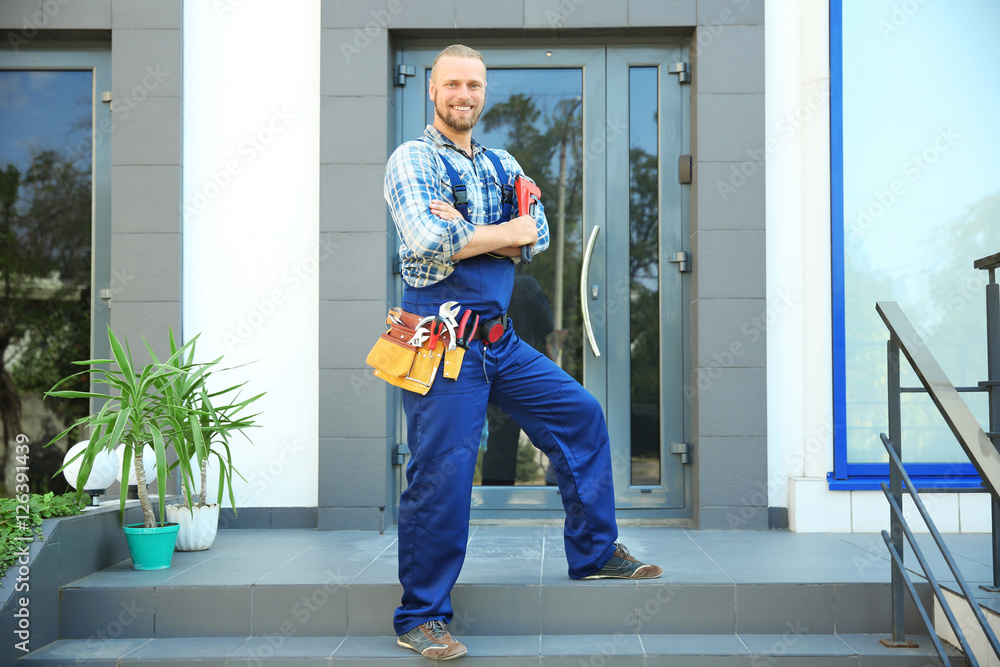 Handsome plumber with pipe wrench  standing on doorstep
