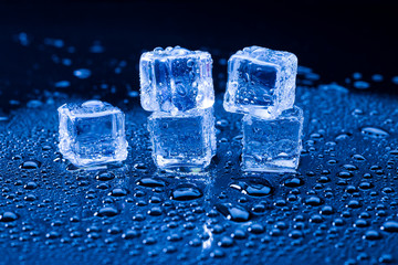 Wet ice cubes and water drop on blue background.