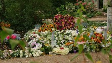 Huge Pile Of Fresh, Colorful Flowers On A Grave. One Bouquet In The Shape Of A Heart.