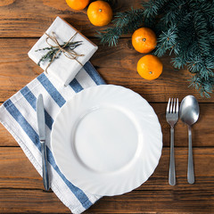 Vintage or rustic christmas table setting from above. Elegant empty white plate, cutlery on linen napkin and natural pine tree branch on rustic planked wood - country style.