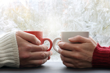 Wall Mural - spend  time together warming favorite drink/ two people hold red and white cup across from a window with frost 