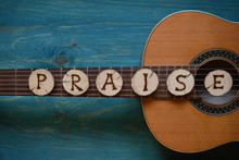 Guitar On Teal Wooden Background With Wood Pieces On It Lettering The Word: PRAISE