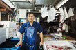 © Mint Images - A traditional fresh fish market in Tokyo. A man in a blue apron standing behind the counter of his stall.