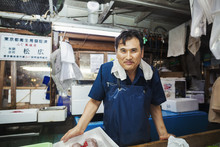 A Traditional Fresh Fish Market In Tokyo. A Man In A Blue Apron Standing Behind The Counter Of His Stall. 