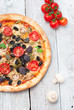 Fresh tasty pizza with asparagus, tomatoes, olives, mushrooms and herbs on a white wooden table. top wiev