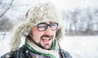 © scharfsinn86 - Adult man with beard wearing glasses. The man smiles. Winter, snow, a man in a fur hat. Man winks