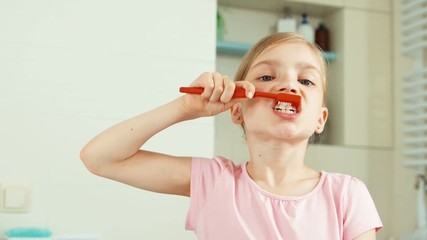 close up portrait child girl 7-8 years old cleaning teeth in bathroom and looking at camera. zooming