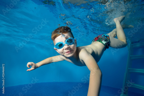 Little boy swims underwater in the pool, smiling, blowing bubbles and ...