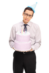 Wall Mural - Sad young man with a party hat holding a birthday cake