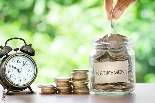 Fotografía Hand putting Coins in glass jar with retro alarm clock , retirement