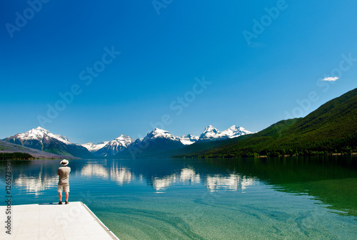 Fotografia, Obraz Man looking at the majestic snow-capped mountains reflecting in the calm waters