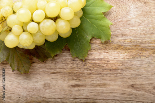 Fototapeta na wymiar Kiść białych winogron i zielonych liści na drewnianym tle