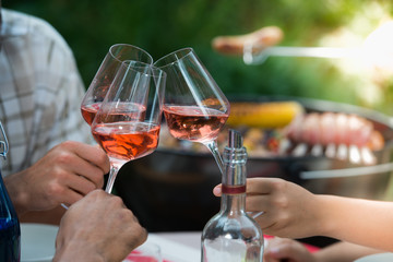 Happy friends having fun outdoors, hands toasting rose wine glass