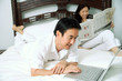 © Alexander - Couple in bedroom, man using laptop, woman reading newspaper