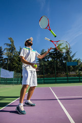 Wall Mural - Professional tennis player juggling with rackets. He is having a good time before starting the game. 