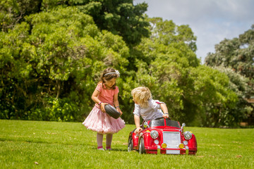 young happy children - boy and girl - driving a toy car outdoors