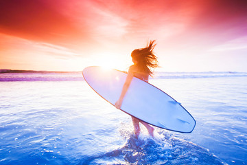 Wall Mural - Surfer girl on beach at sunset