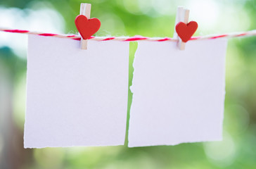 2 Blank white paper and red clip paper heart hanging on the clothesline with bokeh nature background.Designer concept.