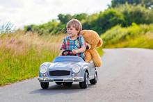 Little Kid Boy Driving Big Toy Car With A Bear, Outdoors.