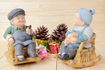  lovely grandparent doll siting rocking bamboo chair with gift boxes and gift decoration christmas on pine wooden background with copy space.