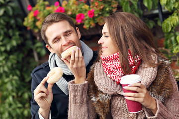 Wall Mural - Young couple sitting on bench with coffee and donuts